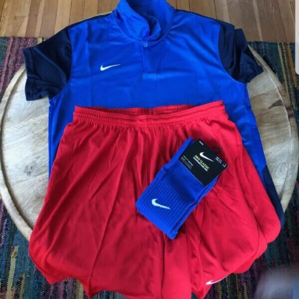 A blue Nike soccer jersey, red Nike shorts, and a pair of blue Nike socks are laid out on a round wooden table.