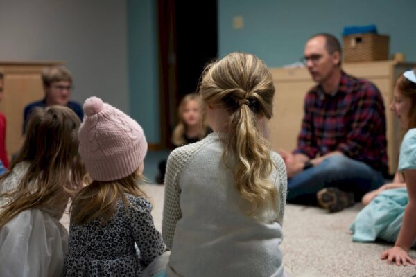 Children and an adult sit in a circle, talking in a cozy, indoor room.
